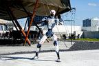 Unitree R1 Humanoid boxing mode and standing in front of an old airplane with modern buildings in the background.