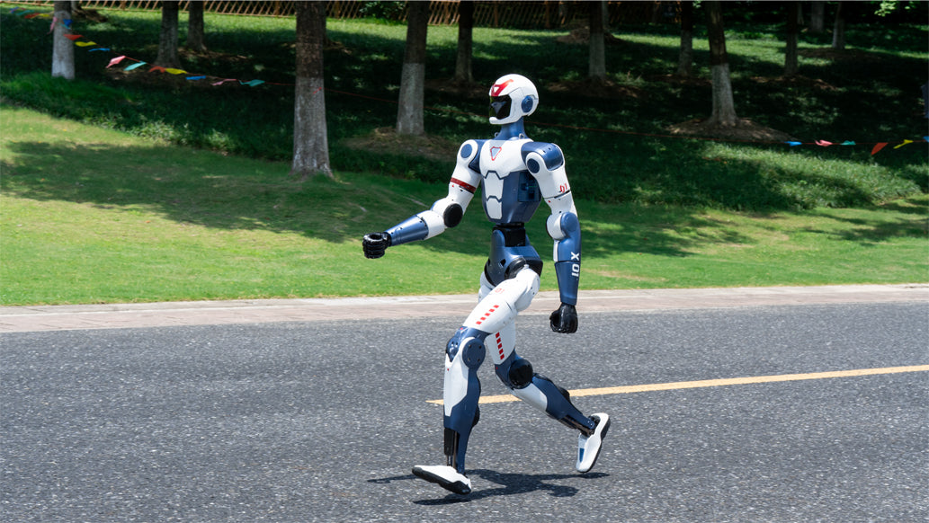 Unitree R1 Robot walking on a road with trees and grass in the background
